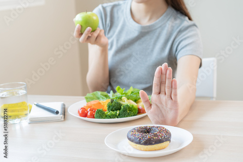Diet  Dieting asian young woman or girl use hand push out  deny sweet donut and choose green salad vegetables  eat food for good healthy  health when hungry. Close up female weight loss person.