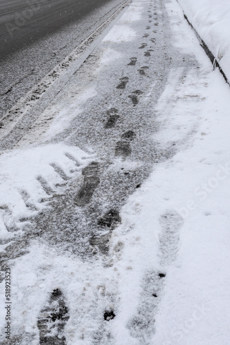 Footprints on fresh white snow at sidewalk. Asphalt covered with snow in winter season. Selective focus © Yulia
