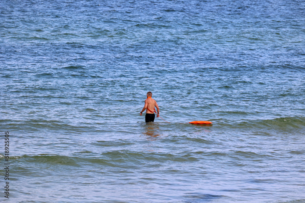 Ratownik na plaży podczas patrolowania brzegu wody.  - obrazy, fototapety, plakaty 