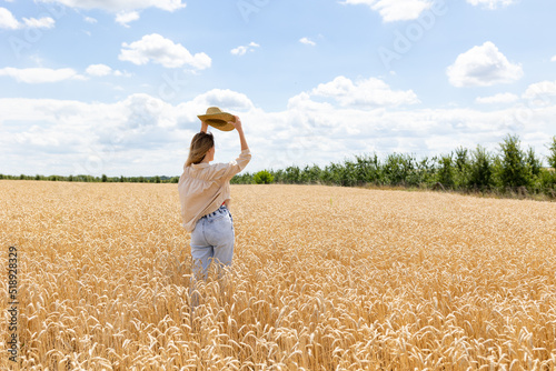 Back view of woman in big hat walking on wheat field in summer at ripe wheat ears. girl enjoying peacefulness and beautiful nature.