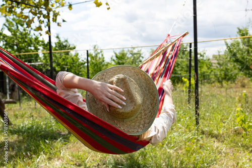 back view of woman in summer day wearing hat taking a nap in the hammock in her backyard relaxing