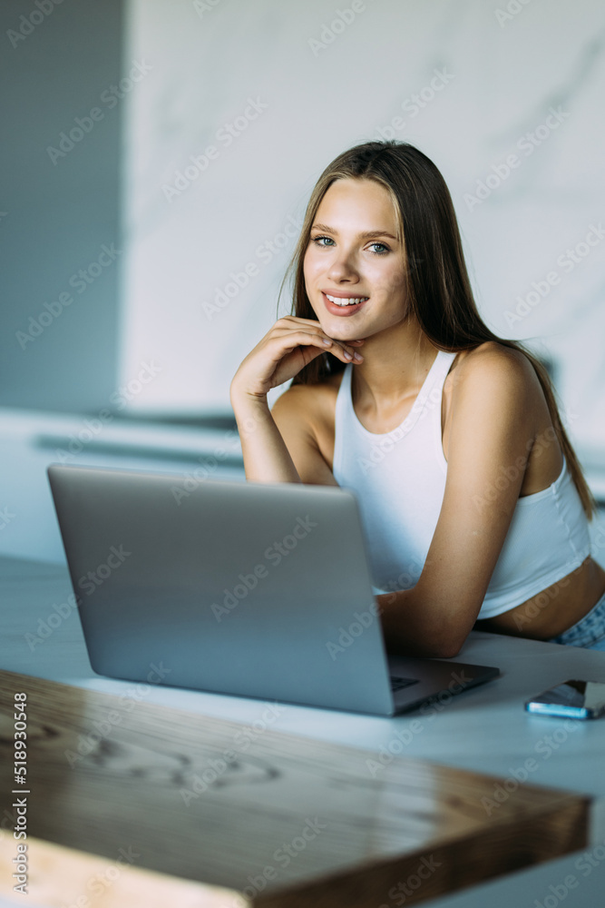 Young woman looking her laptop while holding a cup of coffee in the kitchen at home. Young woman looking her laptop while holding a cup of coffee in the kitchen at home.