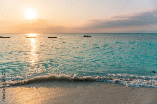 NUNGWI, Zanzibar. Beautiful sunset at the beach in Tanzania, Africa. Turquoise sea, orange sky. Fishing boats in the horizon.