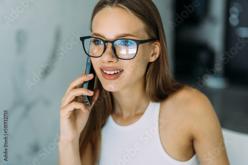 Freelance woman working from home, sitting at kitchen table, using laptop and having phone conversation, looking at computer screen. Remote job concept