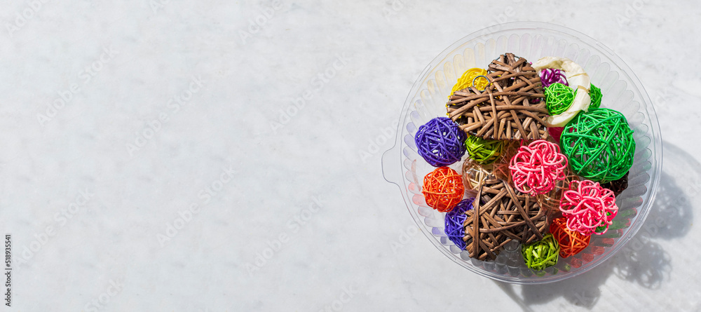 On light surface of table there is plastic container with decorative figurines - multi-colored balls and hearts. Negative space on left.