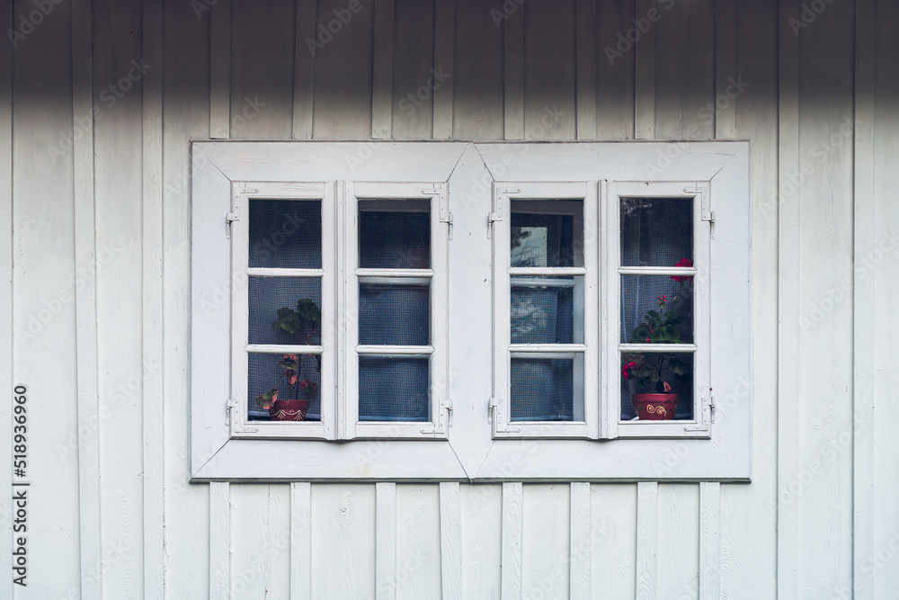 A detail of a white window against a white facade made of wooden planks. Country window