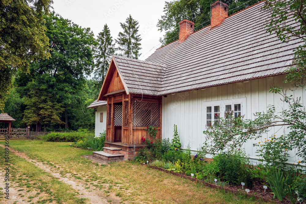 charming country cottage with a shingle roof and a porch and a small garden. Zwierzyniec, Poland