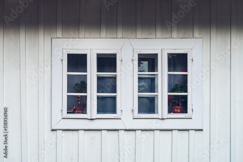 A detail of a white window against a white facade made of wooden planks. Country window