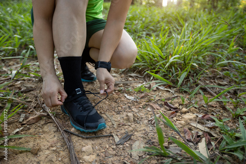 Woman trail runner tying shoelace in forest