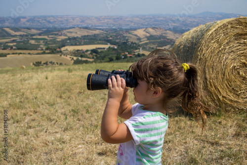 Image of an adorable little girl in the open field as she looks at the horizon with binoculars.