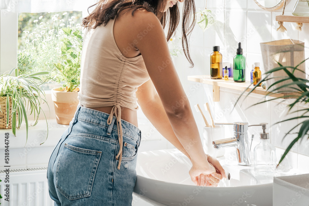 Unrecognisble woman with dark skin washing hands in light bathroom. Natural cosmetics, slef care and wellness concept Unrecognisble woman with dark skin washing hands in light bathroom. Natural cosmetics, slef care and wellness concept