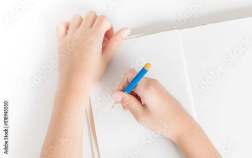Hands of little kid hold the pencil and drawing on the blank book