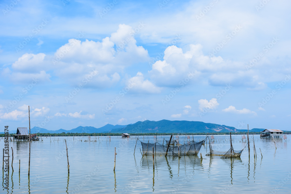 Beautiful view of Songkhla lake that is located in the southern of Thailand with a few of hut as foreground and mountains, blue sky and white cloud as background. Cool tone. Analogous color.