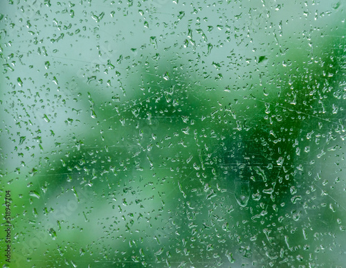 Closeup view of beautiful background of water drops pattern on scratched window glass while raining with blurry tree outside. Cool tone.