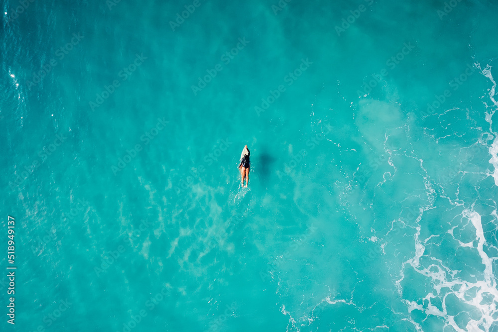 Surf girl on surfboard in blue ocean waiting wave. Aerial view