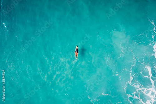 Surf girl on surfboard in blue ocean waiting wave. Aerial view