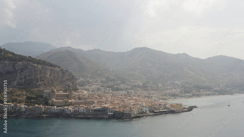 Aerial panoramic view of a coastal town near the mountains on cloudy sky background. Action. Beautiful landscape of the sea shore and small town.