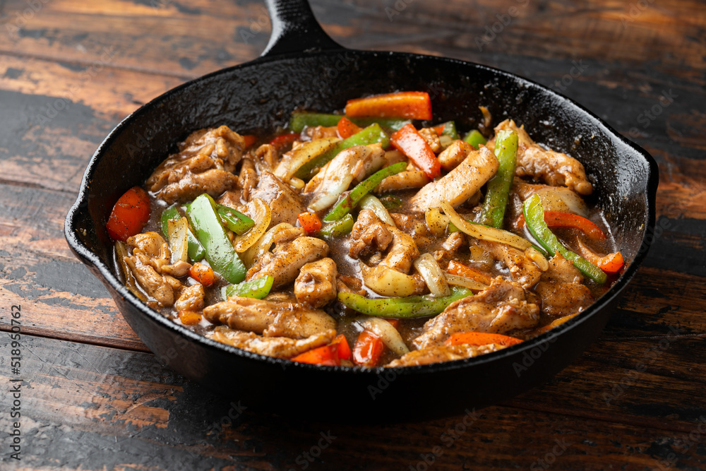 Stir fry pepper chicken with sweet peppers, onion, garlic and ginger in iron cast pan