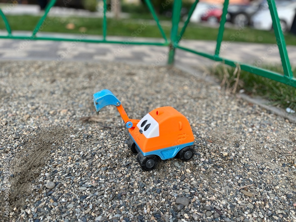 Vivid plastic orange toy excavator with a blue grab bucket on a gravel. Small excavator digs the gravel soil Vivid plastic orange toy excavator with a blue grab bucket on a gravel. Small excavator digs the gravel soil