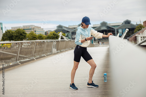 Young healthy sporty woman using cell phone during rest after jog standing on bridge