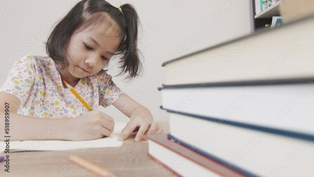 Adorable asian girl is doing her homework on the table with a lot of books and pencil. It shows concept of smart and clever child learning by herself to gain knowledge which is basic education. Adorable asian girl is doing her homework on the table with a lot of books and pencil. It shows concept of smart and clever child learning by herself to gain knowledge which is basic education.