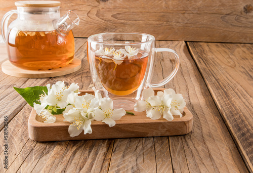 glass transparent cup with fragrant jasmine tea on a wooden tray with the flowers of the plant. wooden rustic table with teapot. tea composition.
