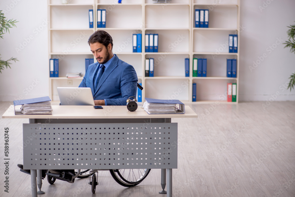 Young male employee in wheel-chair sitting in the office Young male employee in wheel-chair sitting in the office