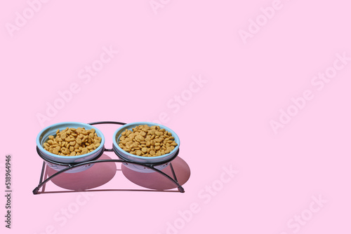 Cat dry food in a bowl on a stand on a pink background. Two bowls of cat food. The concept of a diet for pets, the choice of food for cats. Copy space, minimalism.