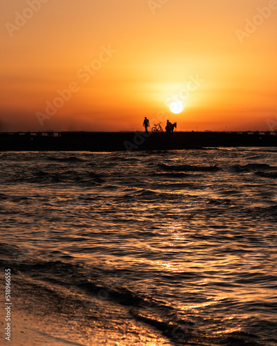 Silhouette of two men and a bike in the beach at sunset