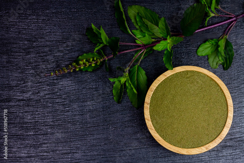 Holy basil powder on wooden bowl with branch on black wooden background, top view. Holy basil leaf are useful herbs and food ingredient has a spicy flavor.