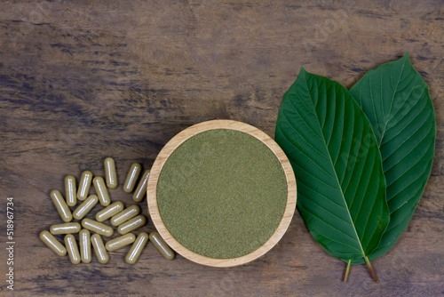 Mitragyna Speciosa Korth or kratom powder on wooden bowl wtih capsules and green leaf on rustic wooden background, top view and copy space. photo