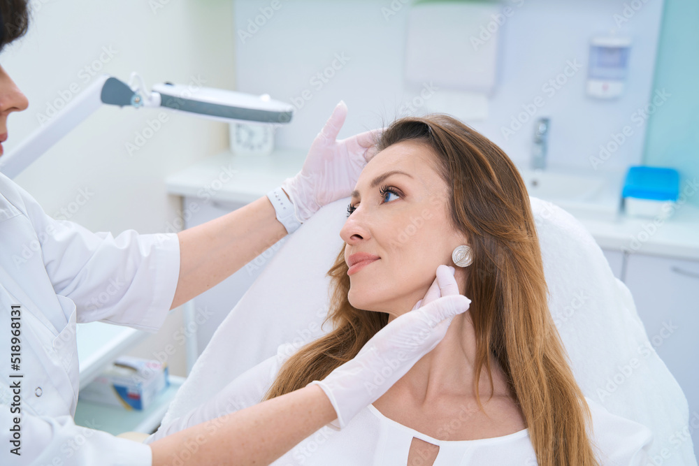 Doctor examining a woman face with both gloved hands