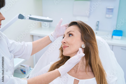 Doctor examining a woman face with both gloved hands