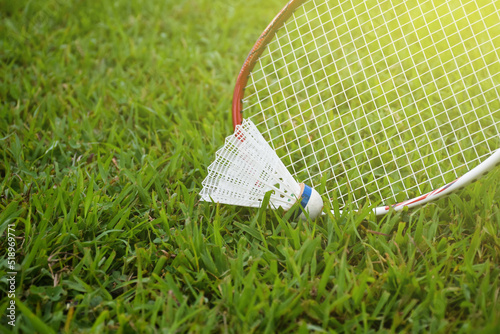 Picking up the badminton shuttlecock on grasslawn by using badminton racket, soft and selective focus on racket and shuttlecock, outdoor badminton playing concept. photo