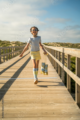 Girl with roller skates at the hands running with happy face through the wooden bridge