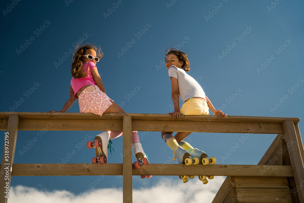 Funny girls turn to the camera while sitting at the wooden bridge - obrazy, fototapety, plakaty 