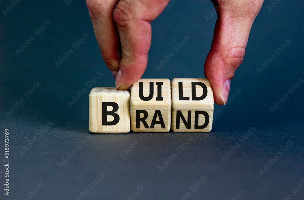 Build your brand symbol. Concept words Build brand on wooden cubes. Businessman hand. Beautiful grey table grey background. Build your brand and business concept. Copy space. Build your brand symbol. Concept words Build brand on wooden cubes. Businessman hand. Beautiful grey table grey background. Build your brand and business concept. Copy space.