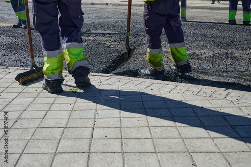 professional workers from an asphalt company working with their shovels and brushes in the last phase of the application of the pavement layer on city streets.
