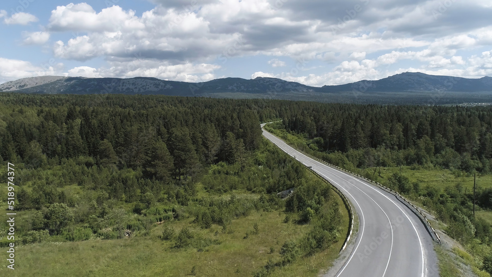 Aerial of the empty road going through forest, summer nature landscape. Scene. Flying above the highway through the green spruce forest on blue cloudy sky background.