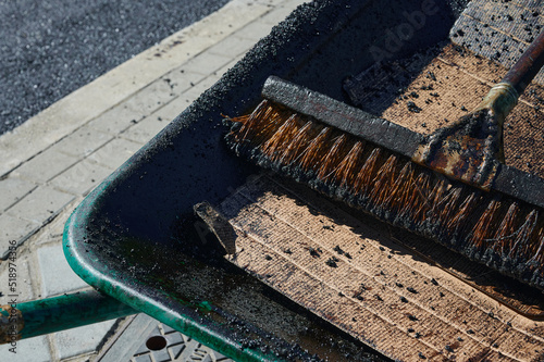 wheelbarrow loaded with a hard brush used by an asphalt company in the last phase of the application of the pavement layer on city streets.