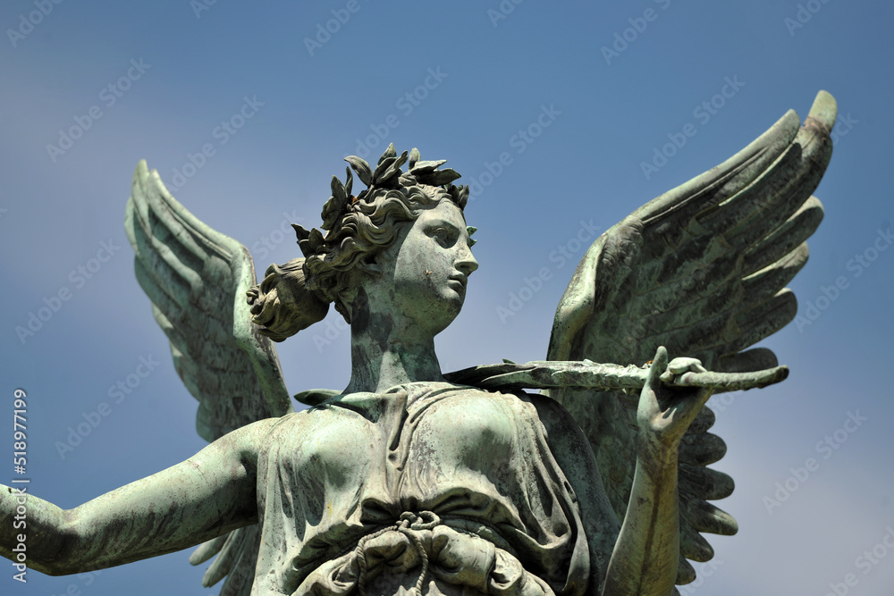 An metal sculpture of an angel in a park in Berlin Germany in front of a blue sky.	