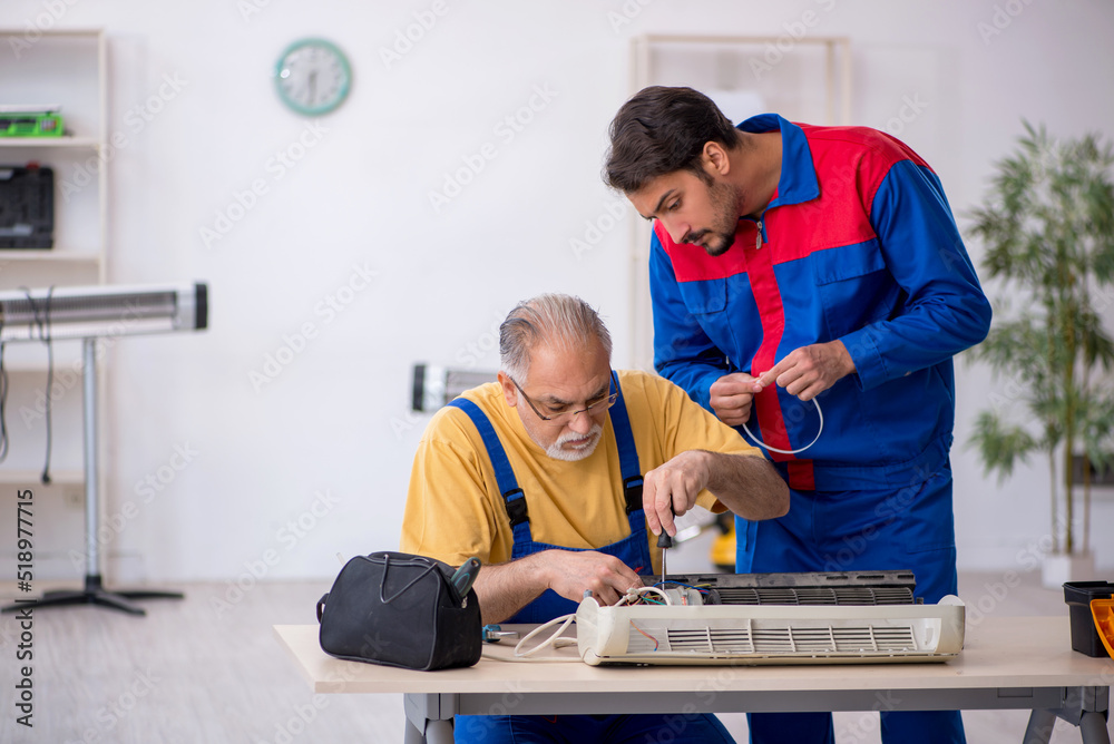 Two male repairmen repairing air-conditioner Two male repairmen repairing air-conditioner