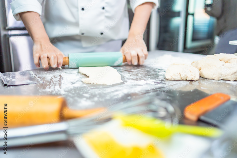 Smiling bakers looking at camera..Chef baker in a chef dress and hat, cooking together in kitchen.Young asian man takes fresh baked cookies out of modern electric oven in kitchen. Smiling bakers looking at camera..Chef baker in a chef dress and hat, cooking together in kitchen.Young asian man takes fresh baked cookies out of modern electric oven in kitchen.
