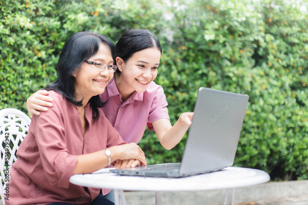 Young happy woman and middle aged senior woman playing laptop together at home garden. Asian daughter and mother shopping online spending time together. mature or elderly with technology Young happy woman and middle aged senior woman playing laptop together at home garden. Asian daughter and mother shopping online spending time together. mature or elderly with technology