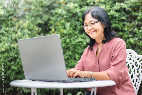 Asian senior woman working on laptop in backyard. 