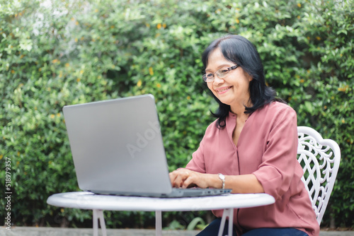 Happy senior woman working online with laptop at home garden. Asian Mature female enjoying surfing internet. Old age people and technology concept.