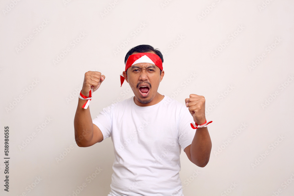 Asian man standing while clenching hand and shouting. Indonesian independence day concept Asian man standing while clenching hand and shouting. Indonesian independence day concept