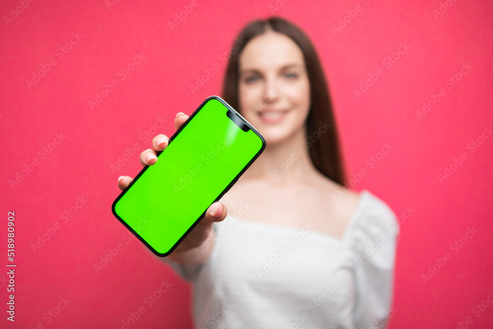 Happy woman standing and hold smartphone on pink background. Green screen phone screen