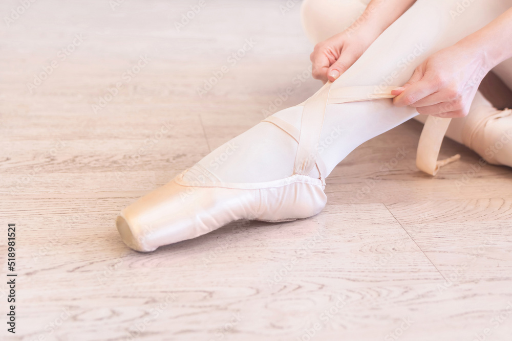 A seated ballerina tightens her pointe shoes