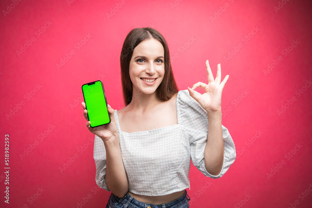 Happy woman standing and hold smartphone and gesting okay on pink background. Green screen phone screen Happy woman standing and hold smartphone and gesting okay on pink background. Green screen phone screen